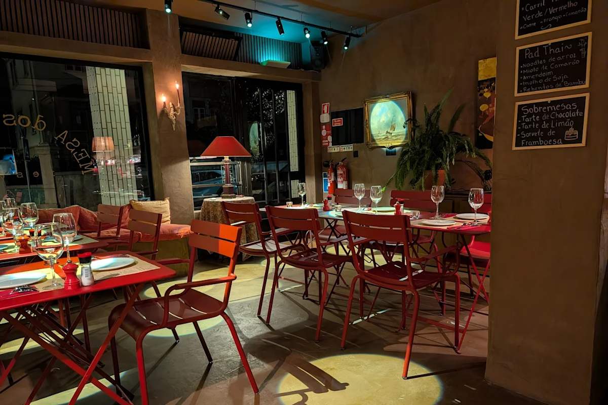 Interior do restaurante com cadeiras metálicas coloridas, plantas decorativas e menu em ardósia
